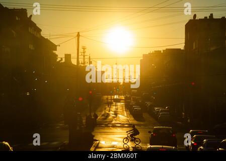 Scène urbaine. Les voitures se tiennent au feu. Silhouettes à vélo et à pied sur la rue piétonne, dans un coucher de soleil doré. Ombres, silhouettes à Banque D'Images