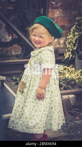 Vue rétro de la petite fille isolée souriant dans les années 1940 habillez comme 1940 enfant de la guerre WW2 Grande-Bretagne, 1940 chemin de fer patrimoine Royaume-Uni événement d'été. Banque D'Images