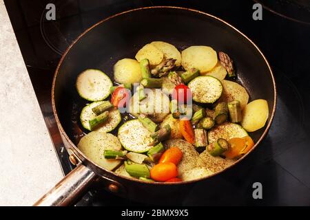 Faire une casserole sur une plaque chauffante avec des pommes de terre, des courgettes, des petites tomates de vigne et des asperges vertes Banque D'Images