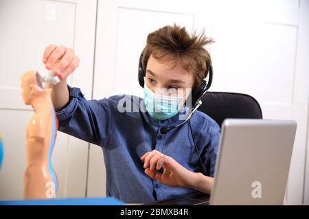 Enseignement à distance en ligne. École en masque médical étudiant à la maison, travaillant à l'ordinateur portable et faisant des devoirs à l'école. Coronavirus quar Banque D'Images