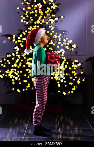 Un petit garçon se place et décorent le salon de l'arbre de Noël en portant le costume de fête de l'elfe le soir Banque D'Images