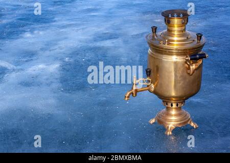 Un magnifique samovar en cuivre brillant se tient sur la glace avec un espace de copie. Une bouilloire russe travaille sur le bois de chauffage. Magnifique glace bleue. Horizontale. Banque D'Images