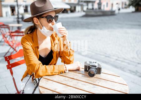 Jeune femme au masque facial, assise sur la terrasse du café seule. Concept de distanciation sociale et nouvelles règles sociales après la pandémie du coronavirus. Banque D'Images
