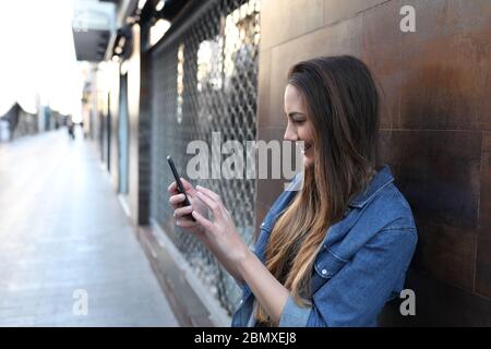 Vue latérale d'une fille heureuse vérifie le smartphone dans la rue Banque D'Images