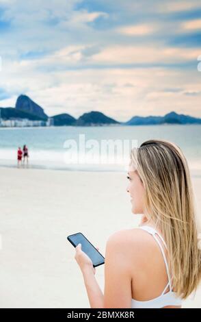 Une jeune femme utilisant son téléphone mobile sur la plage de Rio Banque D'Images