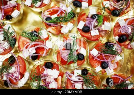 Salade de tomates, concombres, oignons, olives, persil et chés Feta disposés en verres sur une table dorée Banque D'Images