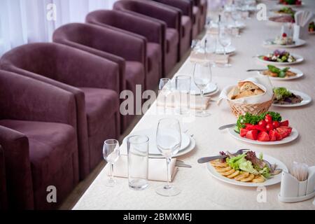 une table recouverte d'une nappe blanche avec des salades, des verres, des assiettes, des serviettes et un certain nombre de sièges Banque D'Images