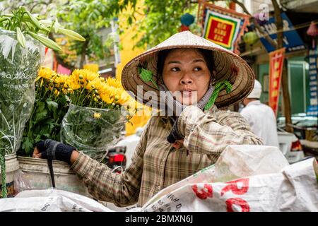 Une jeune femme regarde dans son marché aux fleurs dans les rues de Hanoi, Vietnam Banque D'Images
