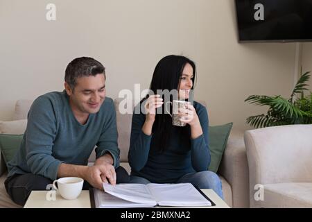 Homme et femme dans le salon assis sur des canapés confortables beige, étudiant des documents et buvant du café. Banque D'Images