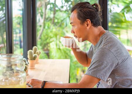 Homme asiatique tenant une tasse de café à la main et boire fond cactus mis sur la table. Banque D'Images