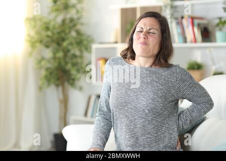 Femme adulte en douleur se plaignant de mal de dos assis sur un canapé à la maison Banque D'Images