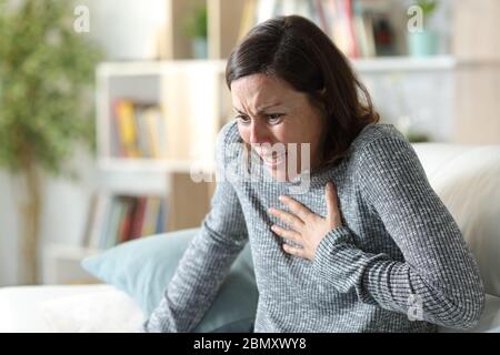 Femme adulte effrayée souffrant d'une crise cardiaque touchant la poitrine dans la douleur assise sur un canapé à la maison Banque D'Images