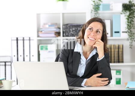 Une femme de direction pensive qui pense regarder vers le haut imaginer s'asseoir sur un bureau au bureau Banque D'Images