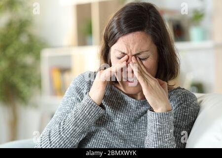 Femme d'âge moyen souffrant de fatigue oculaire assise sur un canapé à la maison Banque D'Images