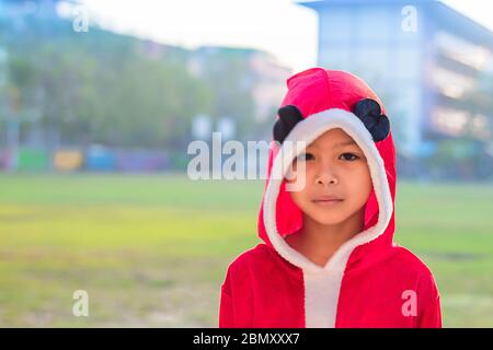 Un garçon asiatique portant un fond de Noël rouge sur la pelouse de l'école. Banque D'Images