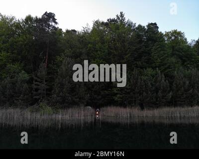 Vue aérienne de 2 personnes tente camp au lac vert avec feu de camp au coucher du soleil. Banque D'Images