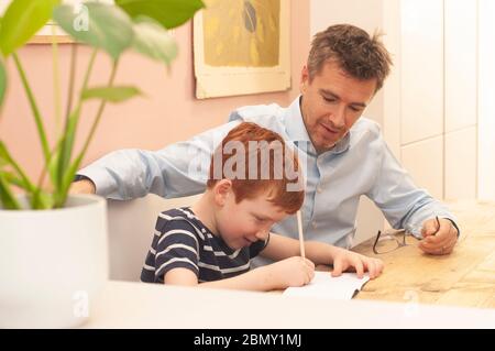 Papa aide pré-adolescent garçon avec son travail d'école à la maison pendant le homeschooling en raison du blocage du coronavirus. Format paysage. Banque D'Images