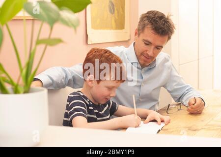 Papa aide pré-adolescent garçon avec son travail d'école à la maison pendant le homeschooling en raison du blocage du coronavirus. Format paysage. Banque D'Images