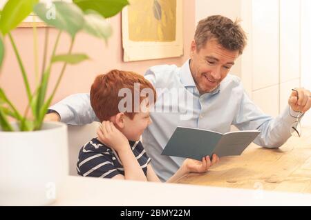 Papa aide pré-adolescent garçon avec son travail d'école à la maison pendant le homeschooling en raison du blocage du coronavirus. Format paysage. Banque D'Images