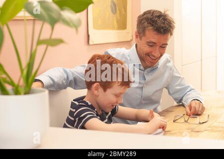 Papa aide pré-adolescent garçon avec son travail d'école à la maison pendant le homeschooling en raison du blocage du coronavirus. Format paysage. Banque D'Images