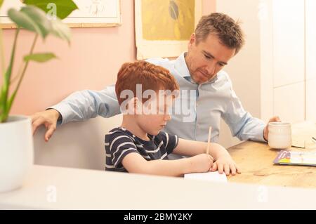 Papa aide pré-adolescent garçon avec son travail d'école à la maison pendant le homeschooling en raison du blocage du coronavirus. Format paysage. Banque D'Images