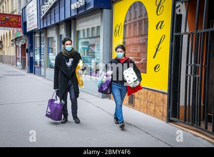 Vienne,Autriche:avril 21,2020: Jeune couple souriant avec masques protecteurs marchant avec du papier toilette et des sacs de shopping le long d'une route pave à Vienne Banque D'Images