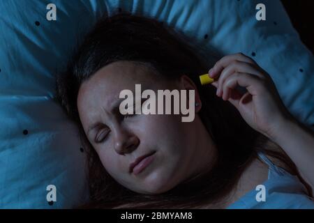 Jeune femme mettant des bouchons d'oreille dans ses oreilles pour la réduction du bruit avant le sommeil, l'insomnie Banque D'Images