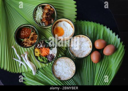 Plats coréens savoureux Bibimbap et poitrine de porc servis dans le grenaille de pinto vue du dessus avec des ingrédients crus (œufs, champignons) sur la feuille verte Banque D'Images