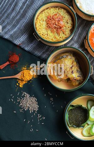 Poulet Biryani élégant avec sauce verte plats indiens dans une boîte repas pinto. Magnifique vue sur le dessus avec épices sur fond vert - tissu indien bleu. Banque D'Images