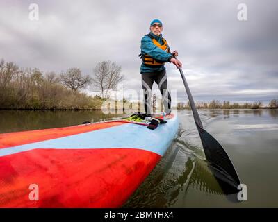 solo senior pagayer masculin avec son stand up paddleboard sur un rivage de lac calme, pagayer solo comme fitness et entraînement avec social distancing, POV de Banque D'Images