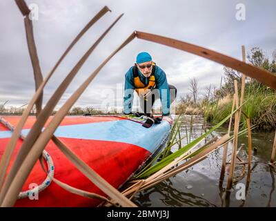 paddler homme senior avec son stand en paddleboard sur un lac calme, paddling solo comme forme physique et entraînement avec distancement social Banque D'Images