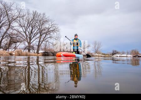 solo lac paddling comme distanciation sociale de loisirs pendant la pandémie de coronavirus, un paddler mâle senior sur stand up paddleboard au début du printemps dans Color Banque D'Images