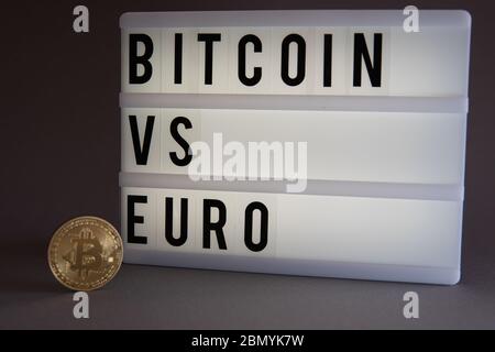 Une pièce de monnaie en Bitcoin dorée se trouve devant un panneau lumineux avec l'inscription Bitcoin vs euro Banque D'Images