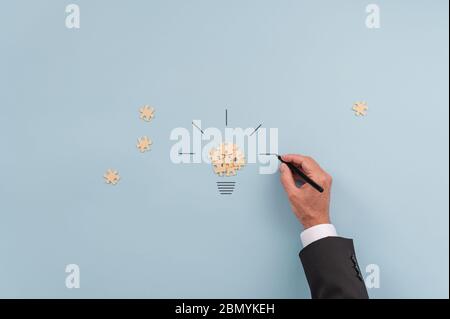 Main d'un homme d'affaires faisant une ampoule de pièces de puzzle et de lignes dessinées à la main. Sur fond bleu. Banque D'Images