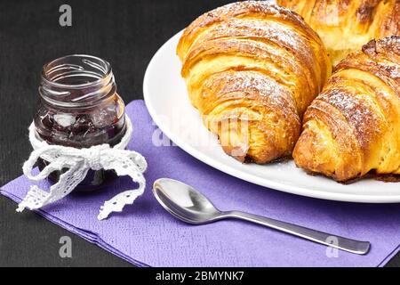 Croissants français en gros plan, jarre de confiture servie sur une serveuse pourpre. Cuisson maison à base de pâte feuilletée. Banque D'Images