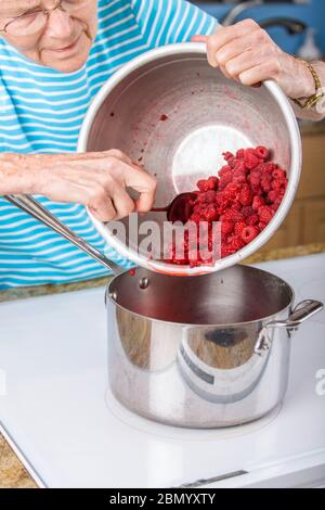 Femme plaçant les framboises dans un pot en préparation pour faire de la confiture. Un lot de confiture de framboises prend quatre tasses de framboises. Banque D'Images