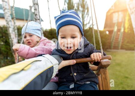 Deux adorables adorables et espiègles frères et sœurs de race blanche garçon fille enfant profiter d'avoir l'amusement balançant balançoire en bois à l'arrière-cour avec le père. Petit tout-petit Banque D'Images