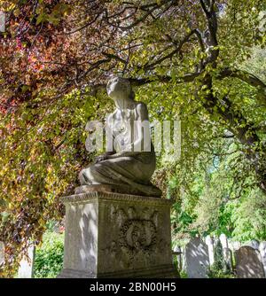 Statue de jeune fille sur pierre tombale avec un écran de feuilles de hêtre en cuivre au cimetière de Brompton, Kensington, Londres. Banque D'Images