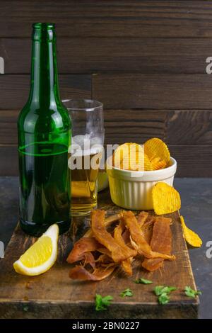 Calmar péruvien avec bière, citron et chips de pomme de terre sur un panneau en bois sombre. En-cas sur le poisson avec de la bière. Gros plan Banque D'Images