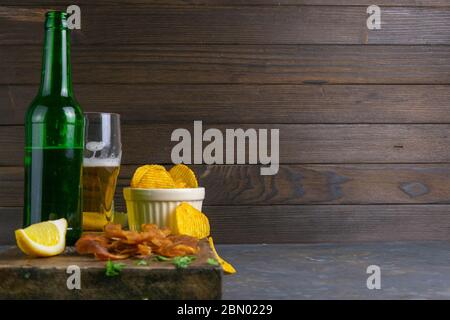 Calmar péruvien avec bière, citron et chips de pomme de terre sur un panneau en bois sombre. En-cas sur le poisson avec de la bière. Vues de face avec espace libre Banque D'Images