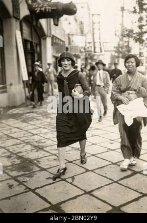 [ années 1920 Japon - Femme japonaise moderne ] — UNE femme japonaise moderne de style occidental avance avec confiance devant le populaire café Tiger (カフェ・タイガー) sur Ginza, Tokyo, ca. 1928. Vers les années 1920, les femmes suivant des modes de vie occidentalisés et des modes de vie émancipés étaient connues sous le nom de Modern Girls (モダンガール, modan garu), généralement raccourcies à Moga (モガ). imprimé gélatine argent du xxe siècle. Banque D'Images