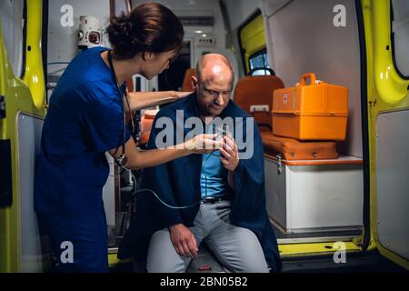 Jeune infirmière donnant un masque d'oxygène à un homme assis en ambulance Banque D'Images