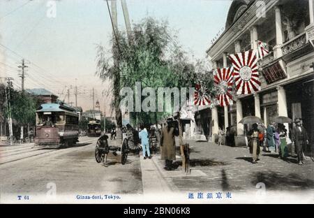 [ 1900s Japon - vue de rue Ginza, Tokyo ] — tramways et piétons sur Ginza à Tokyo, ca. 1907 (Meiji 40). Le bâtiment de droite, avec les drapeaux de soleil levant (旭日旗, Kyokujitsu-ki), est Tenshodo (天賞堂). Dans le fond lointain, la tour historique du bâtiment Hattori (服部時計店ビル) peut être vu. carte postale vintage du xxe siècle. Banque D'Images