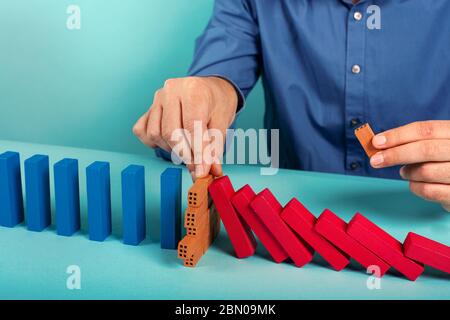 Homme d'affaires arrête une chute de chaîne comme un jeu de domino. Concept de prévention des crises et des échecs dans les affaires. Banque D'Images