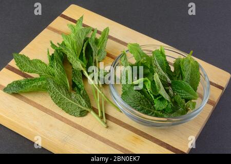 Retirer les feuilles de menthe des petits pains frais crus sur la planche à découper pour les mettre dans un bol en verre Banque D'Images