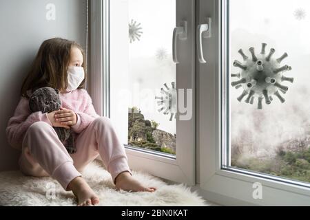 Coronavirus et concept de quarantaine, enfant triste dans le masque médical regarde la fenêtre, petite fille s'assoit sur le seuil de la fenêtre sans danger du virus corona pendant COVID-19 pa Banque D'Images