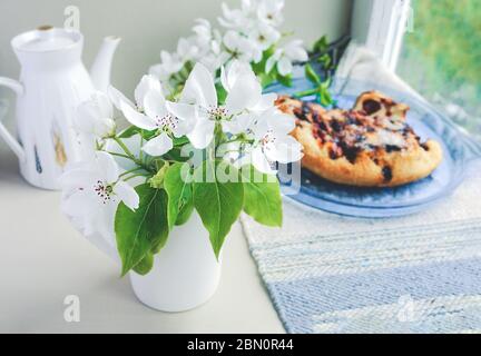 Tasse en porcelaine blanche avec thé vert et fleur de poire blanche fraîche et tarte aux baies maison avec baies sur un plat bleu en arrière-plan. Magnifique Banque D'Images