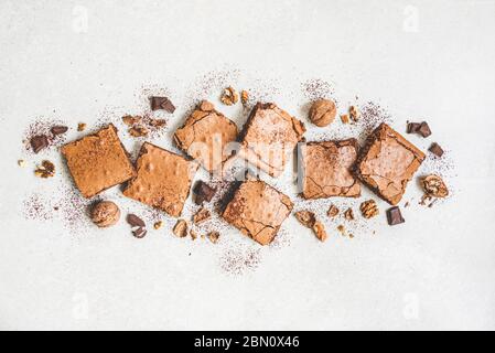 Vue de dessus du gâteau maison au brownie fraîchement préparé avec des noix, du chocolat et de la poudre de cacao sur fond rustique blanc. Banque D'Images