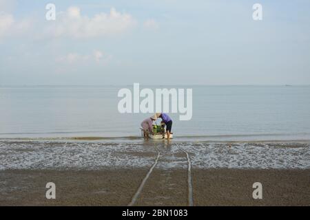 deux hommes sur la plage se préparant à la voile, peut-être pour la pêche en mer; Banque D'Images