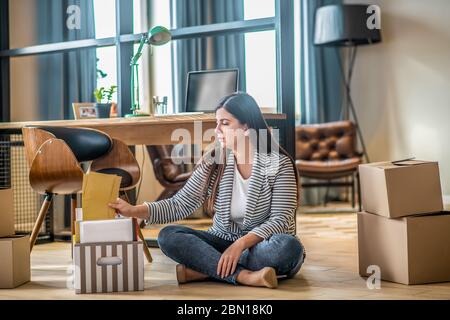 Jeune femme assise sur le sol et emballant ses affaires Banque D'Images